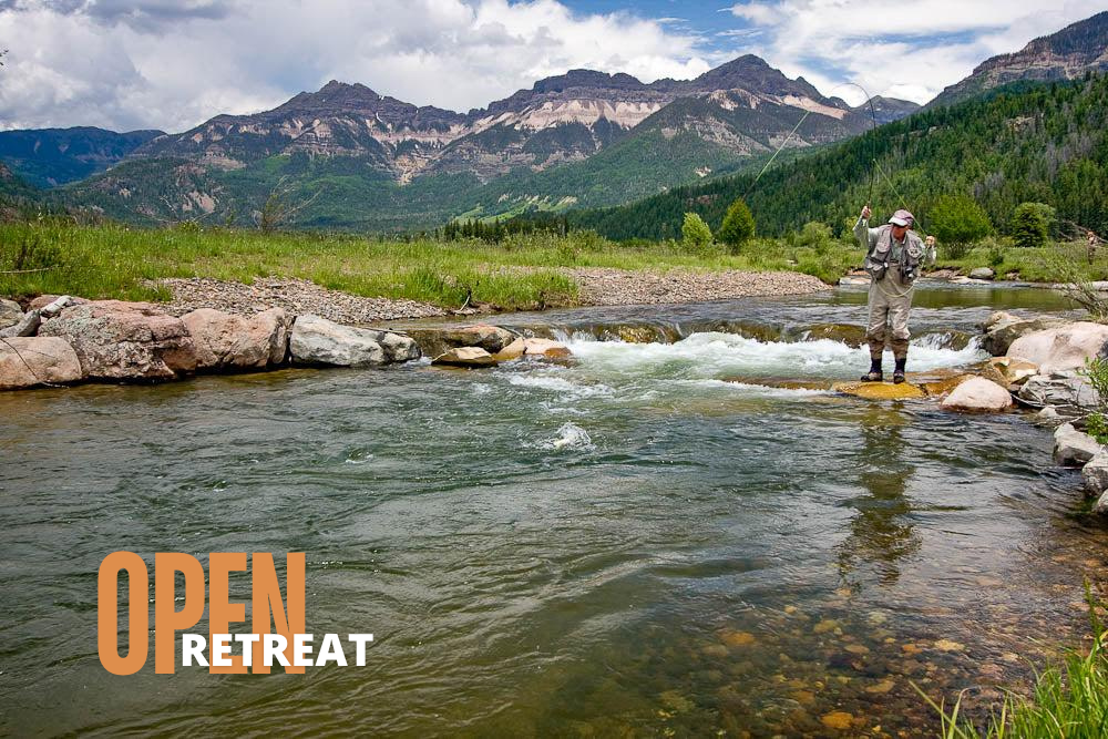 Fly fisherman standing in river with mountains Fly fisherman standing in river with mountains
